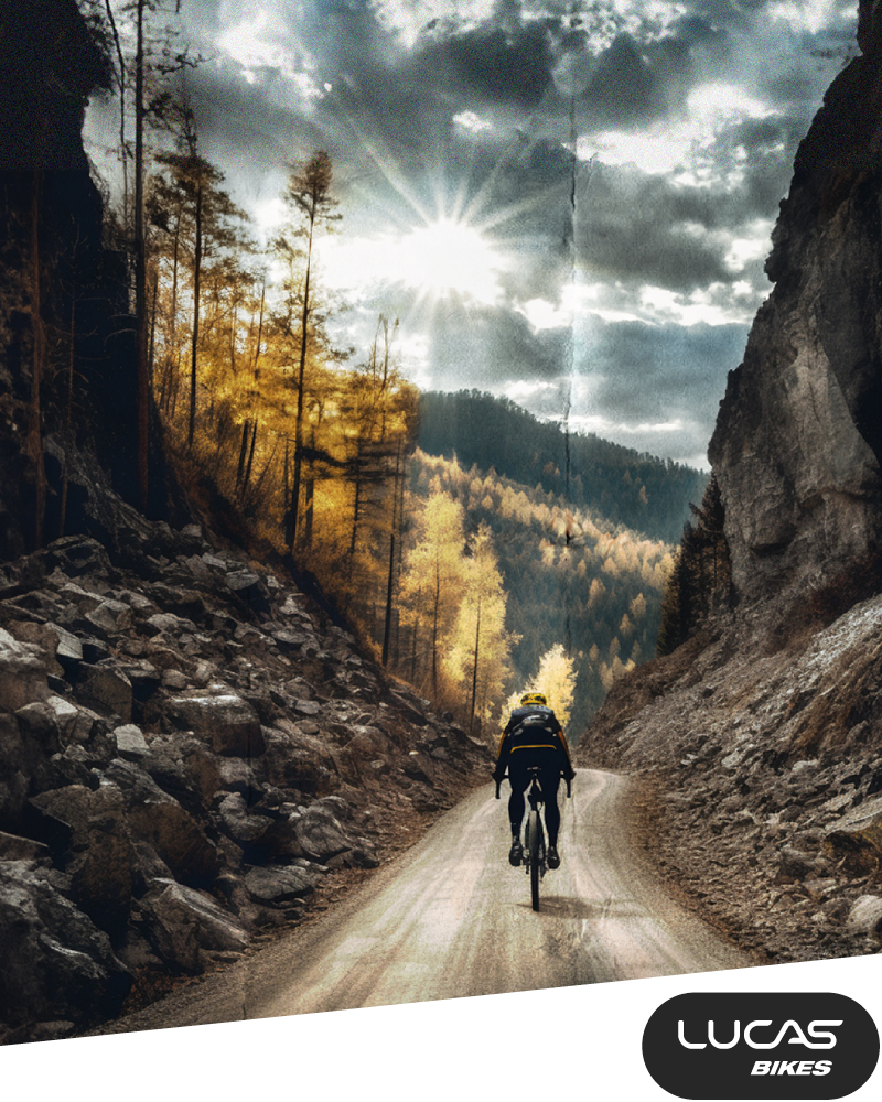 Ein Radfahrer fährt auf einer Bergstraße zwischen felsigen Klippen und herbstlichen Bäumen, während das Sonnenlicht durch dramatische Wolken fällt. Das Logo LUCAS BIKES