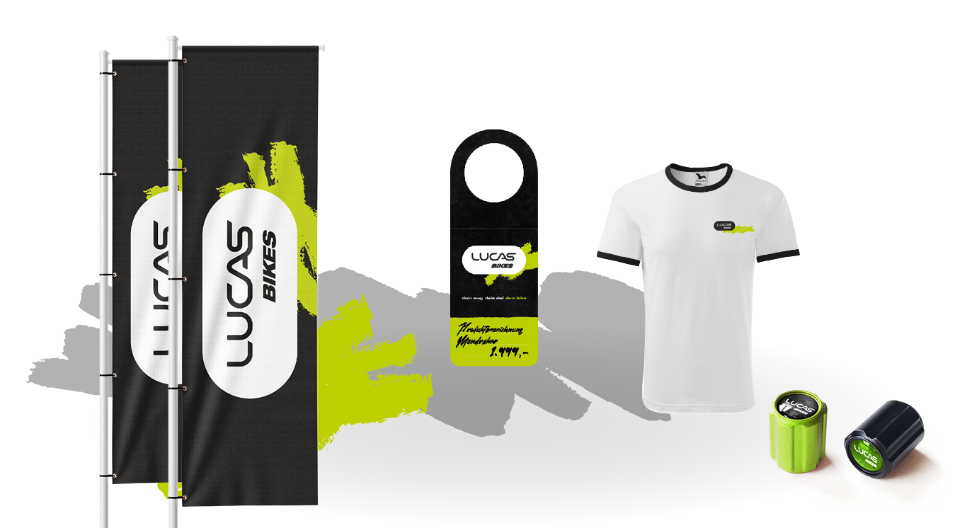 Markenartikel für LUCAS BIKES und die Tanzschule Fischer, darunter zwei schwarze Fahnen, ein T-Shirt, ein Türanhänger und zwei kleine Behälter, alle mit auffälligen Logos mit grünen, schwarzen und weißen Akzenten.