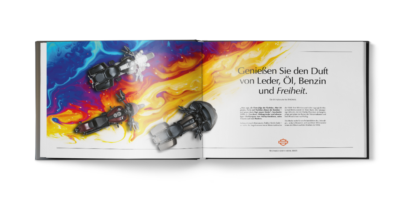 Ein aufgeschlagenes Buch zeigt drei Motorräder vor einem bunten Hintergrund; auf der rechten Seite steht ein deutscher Text über den Duft von Leder, Öl, Benzin und Freiheit.
